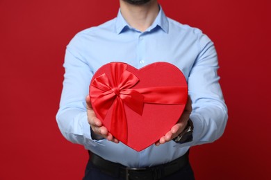 Photo of Happy Valentine's Day. Man with heart shaped gift box on red background, closeup