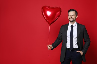 Photo of Happy Valentine's Day. Handsome man with heart shaped balloon on red background. Space for text