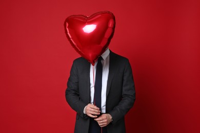 Photo of Happy Valentine's Day. Handsome man with heart shaped balloon on red background