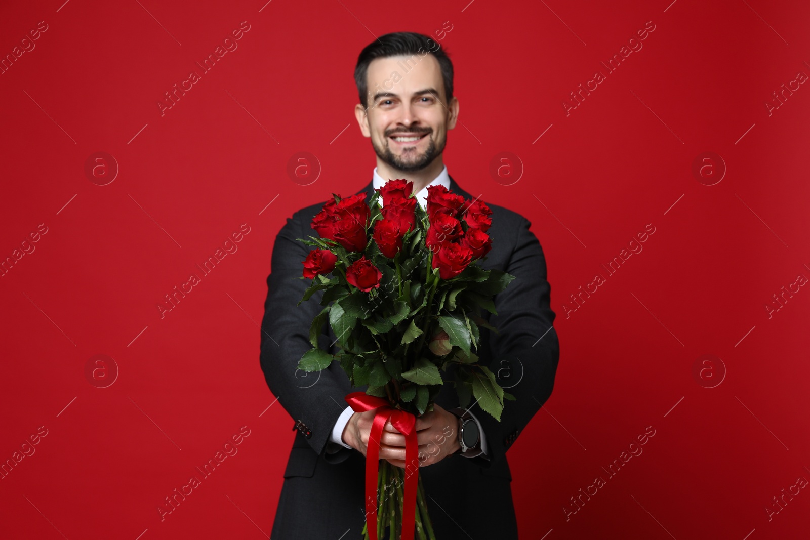 Photo of Happy Valentine's Day. Handsome man with bouquet of roses on red background