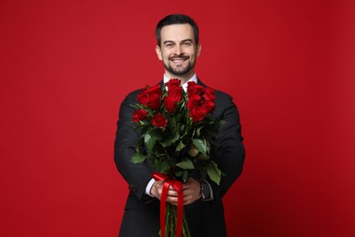 Photo of Happy Valentine's Day. Handsome man with bouquet of roses on red background