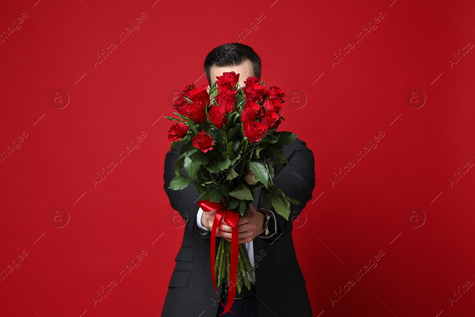 Photo of Happy Valentine's Day. Man with bouquet of roses on red background