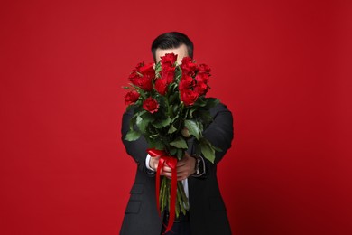 Photo of Happy Valentine's Day. Man with bouquet of roses on red background