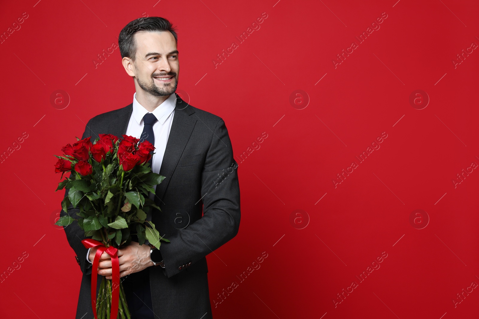 Photo of Happy Valentine's Day. Handsome man with bouquet of roses on red background. Space for text