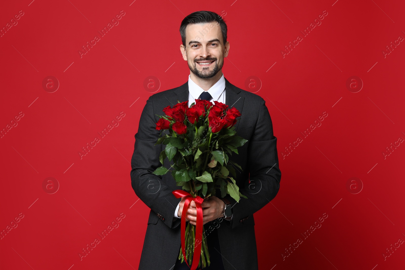 Photo of Happy Valentine's Day. Handsome man with bouquet of roses on red background