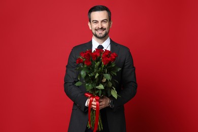 Photo of Happy Valentine's Day. Handsome man with bouquet of roses on red background