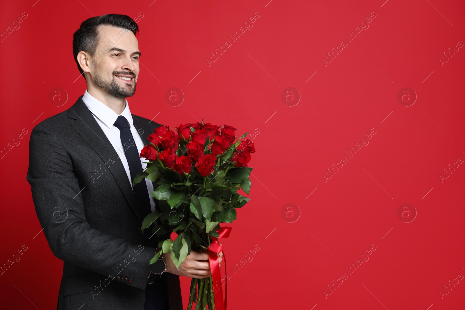 Photo of Happy Valentine's Day. Handsome man with bouquet of roses on red background. Space for text