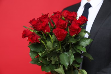 Photo of Happy Valentine's Day. Man with bouquet of roses on red background, closeup