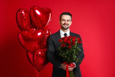 Photo of Happy Valentine's Day. Handsome man with heart shaped balloons and bouquet of roses on red background