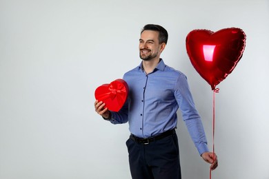 Photo of Happy Valentine's Day. Handsome man with heart shaped balloon and gift on white background. Space for text