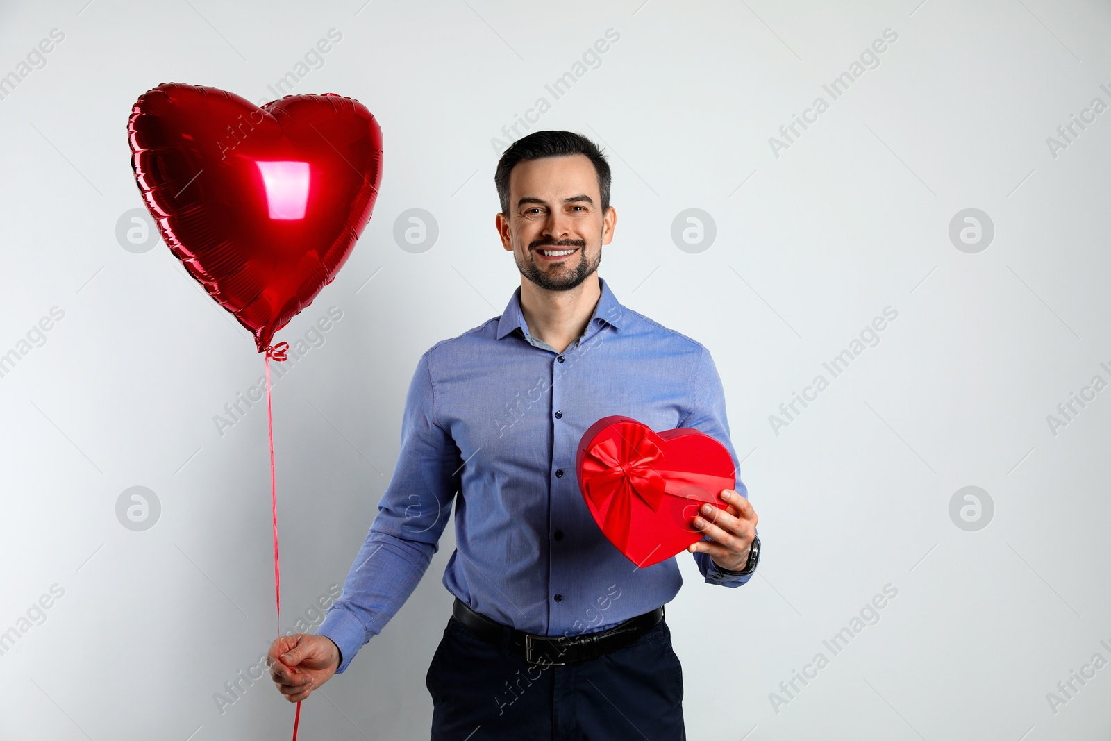 Photo of Happy Valentine's Day. Handsome man with heart shaped balloon and gift on white background