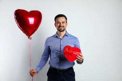 Photo of Happy Valentine's Day. Handsome man with heart shaped balloon and gift on white background