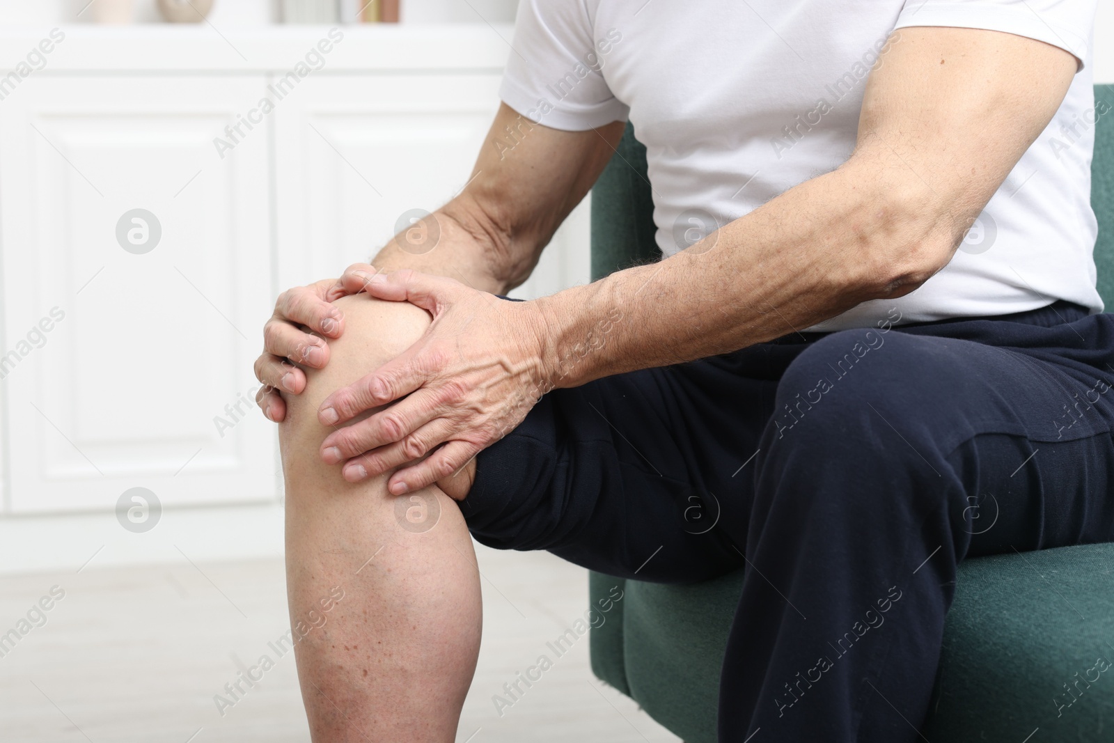 Photo of Senior man suffering from pain in his knee on sofa indoors, closeup