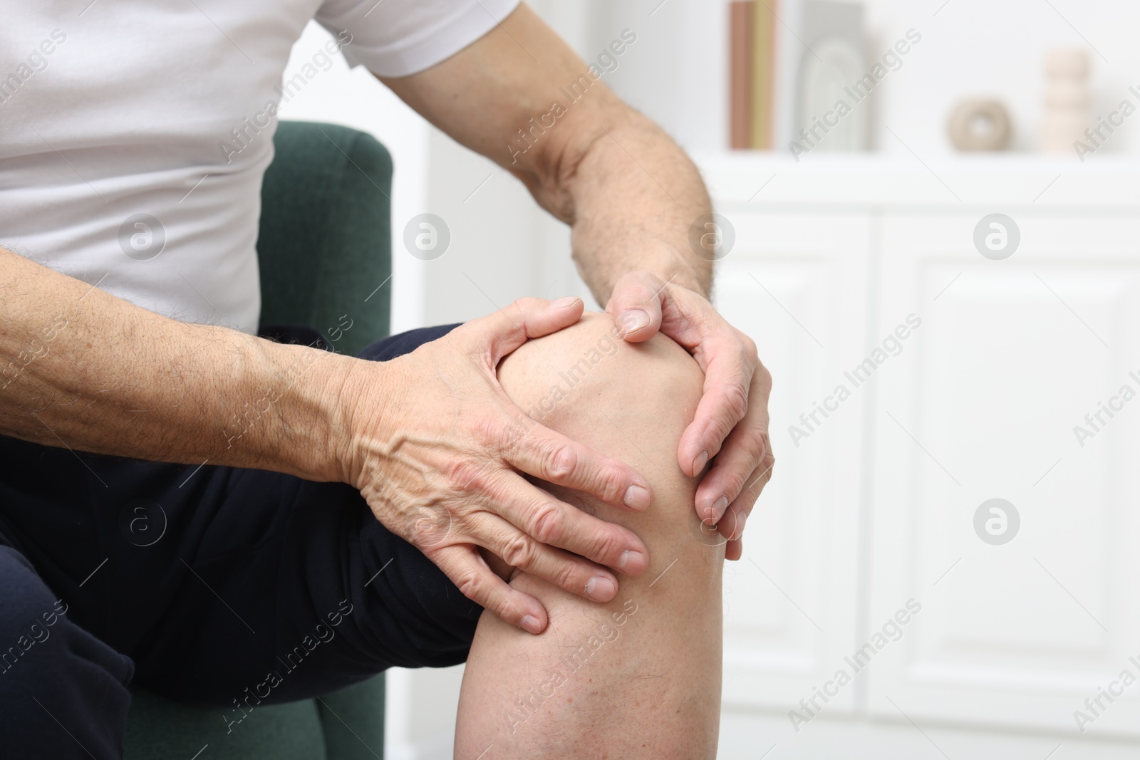 Photo of Senior man suffering from pain in his knee on sofa indoors, closeup