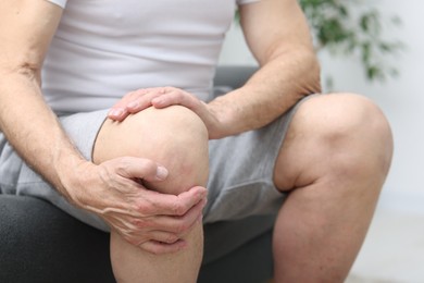 Photo of Senior man suffering from pain in his knee on sofa indoors, closeup