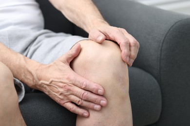 Photo of Senior man suffering from pain in his knee on sofa indoors, closeup