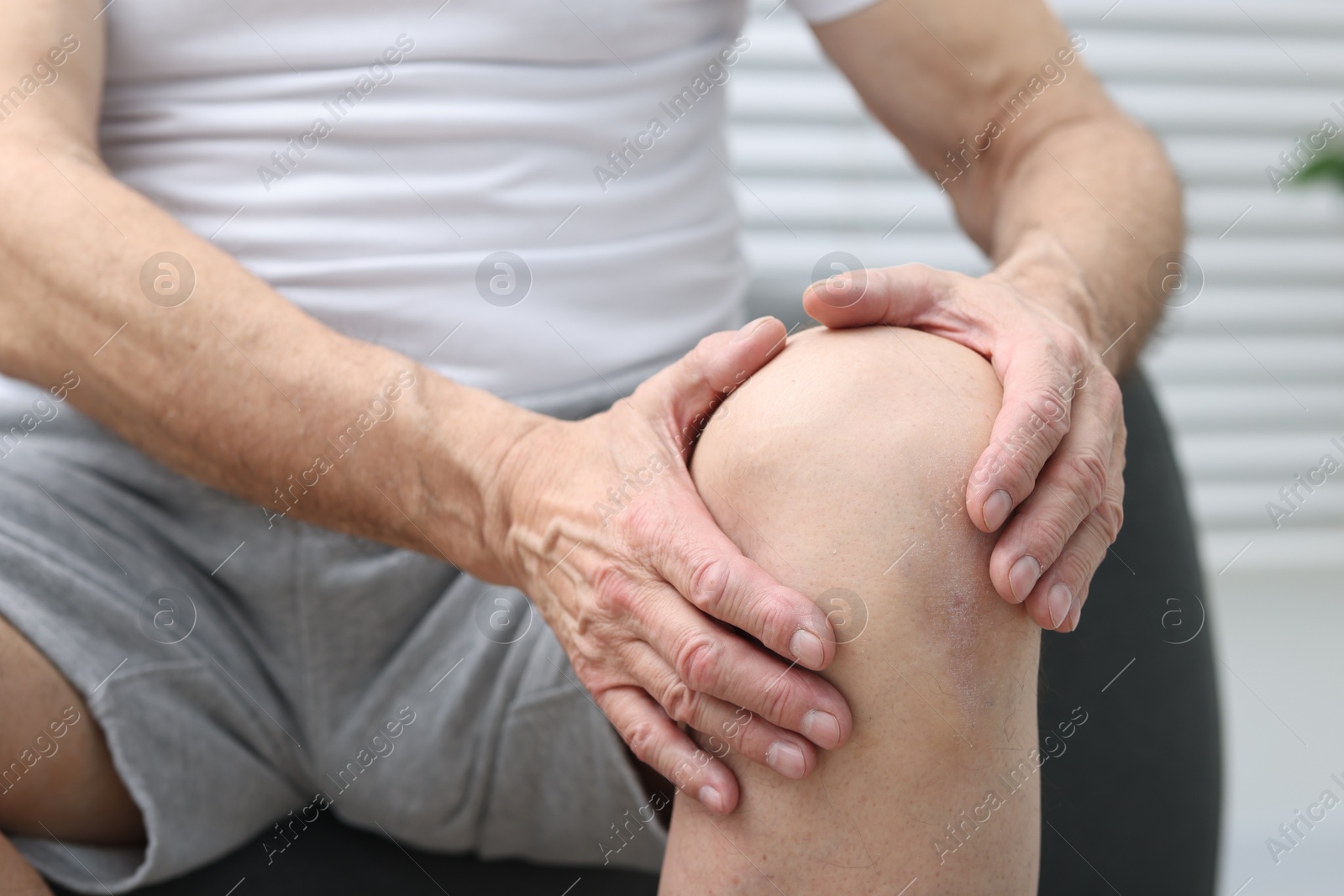 Photo of Senior man suffering from pain in his knee on sofa indoors, closeup