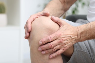 Photo of Senior man suffering from pain in his knee indoors, closeup