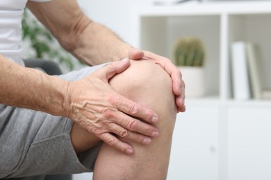 Photo of Senior man suffering from pain in his knee indoors, closeup