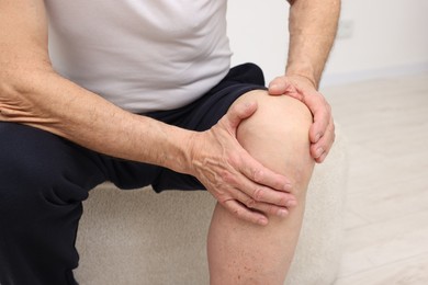 Photo of Senior man suffering from knee pain on pouf indoors, closeup