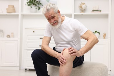 Photo of Senior man suffering from knee pain on pouf at home