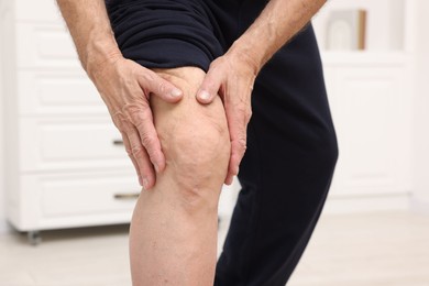 Photo of Senior man suffering from pain in his knee indoors, closeup