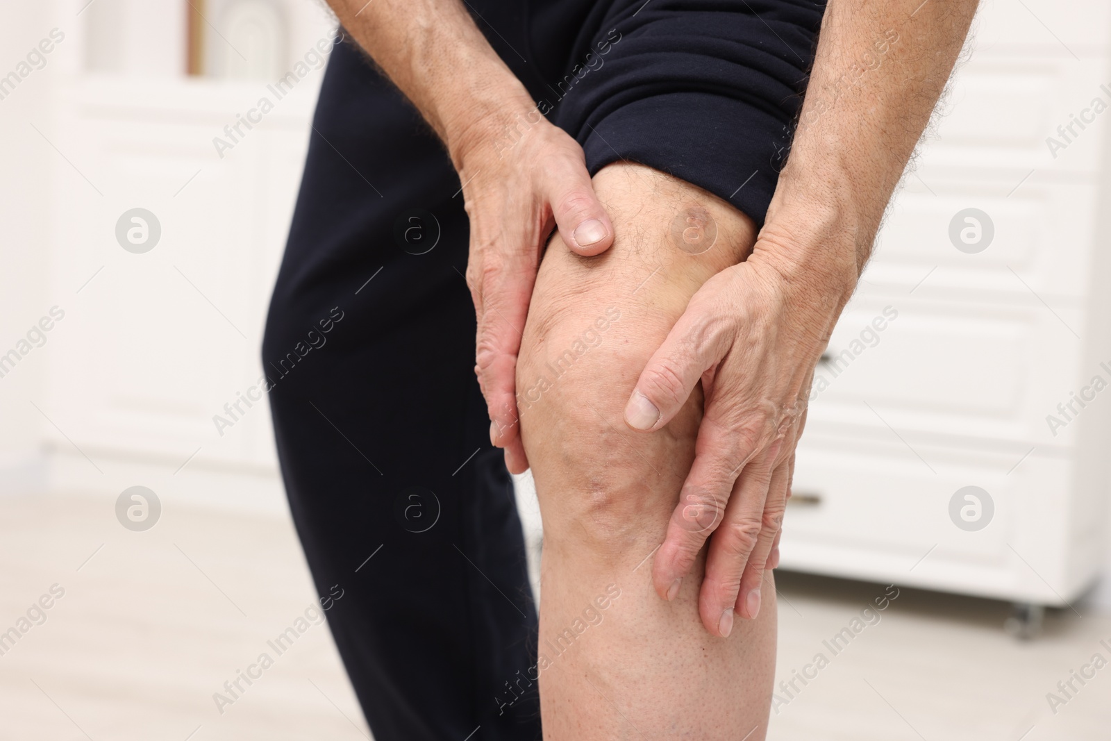 Photo of Senior man suffering from pain in his knee indoors, closeup