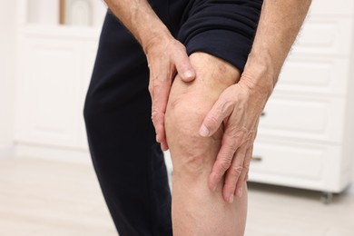 Photo of Senior man suffering from pain in his knee indoors, closeup