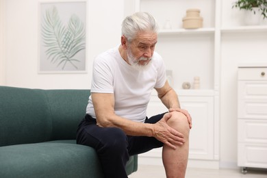 Photo of Senior man suffering from knee pain on sofa at home