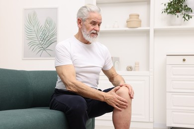 Photo of Senior man suffering from knee pain on sofa at home