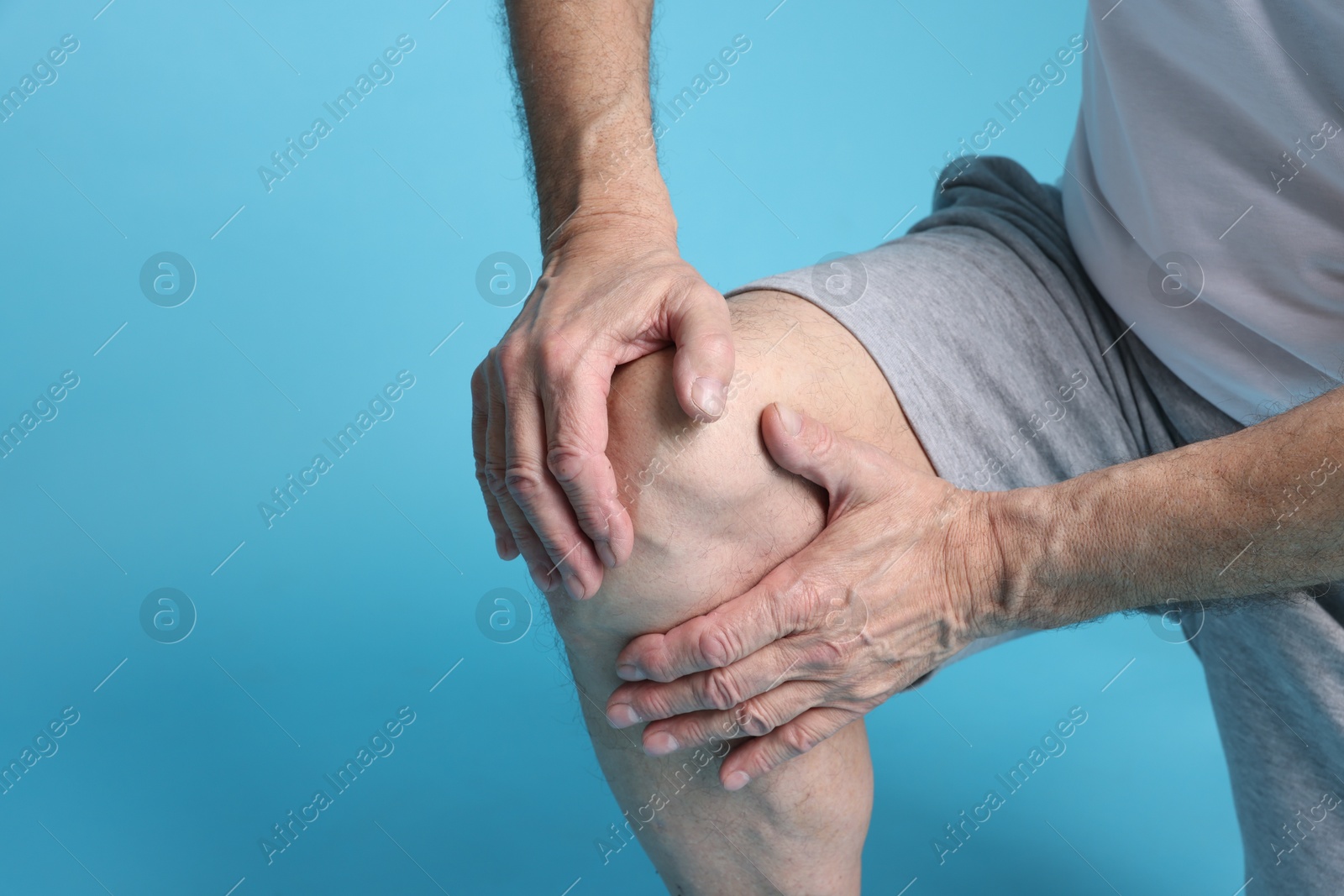 Photo of Senior man suffering from knee pain on light blue background, closeup