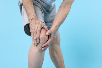 Photo of Senior man suffering from knee pain on light blue background, closeup