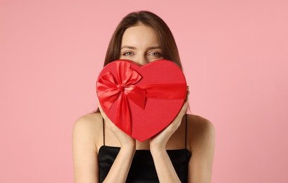 Photo of Happy Valentine's Day. Woman hiding behind heart shaped gift box on pink background