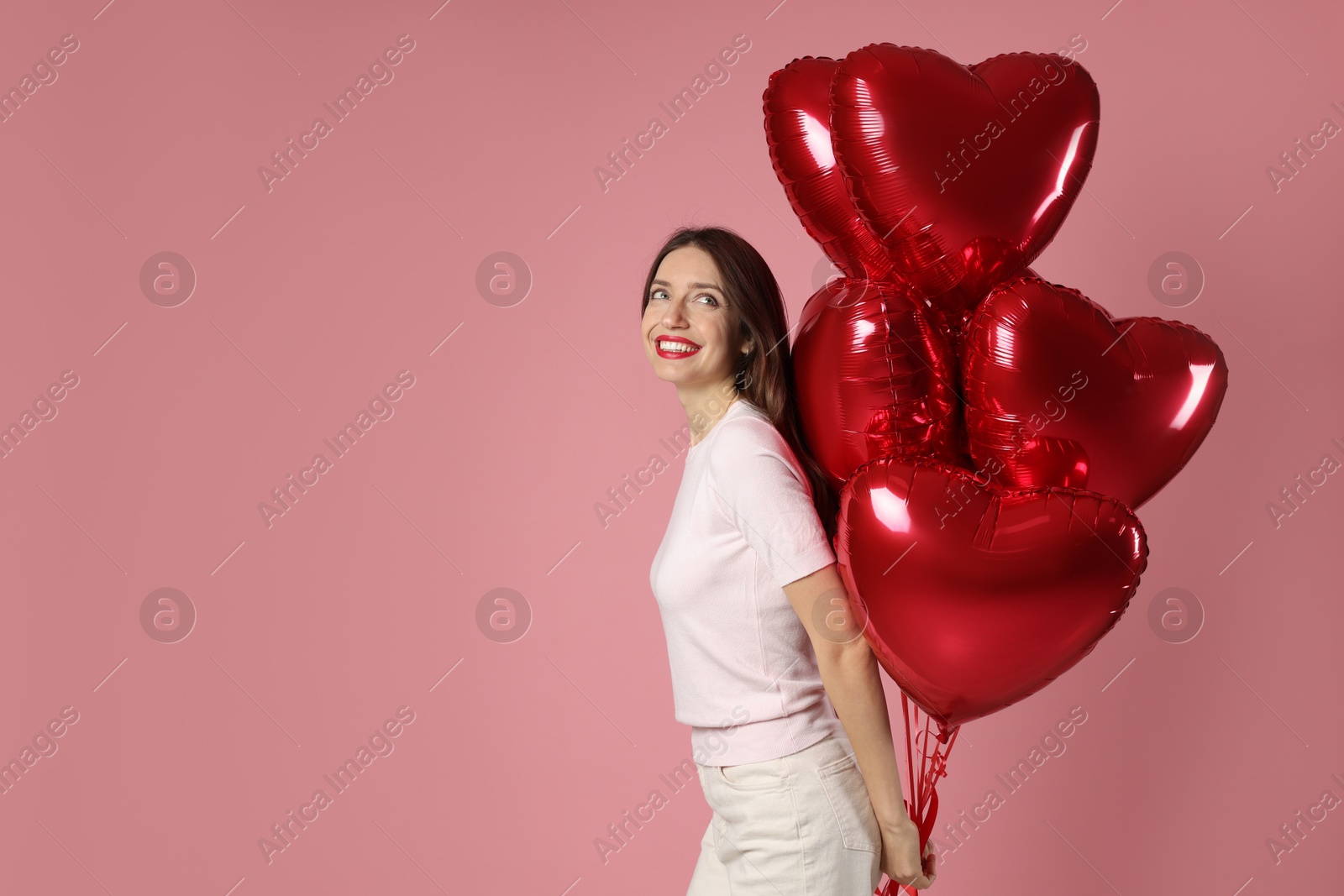 Photo of Happy Valentine's Day. Beautiful woman with heart shaped balloons on pink background. Space for text