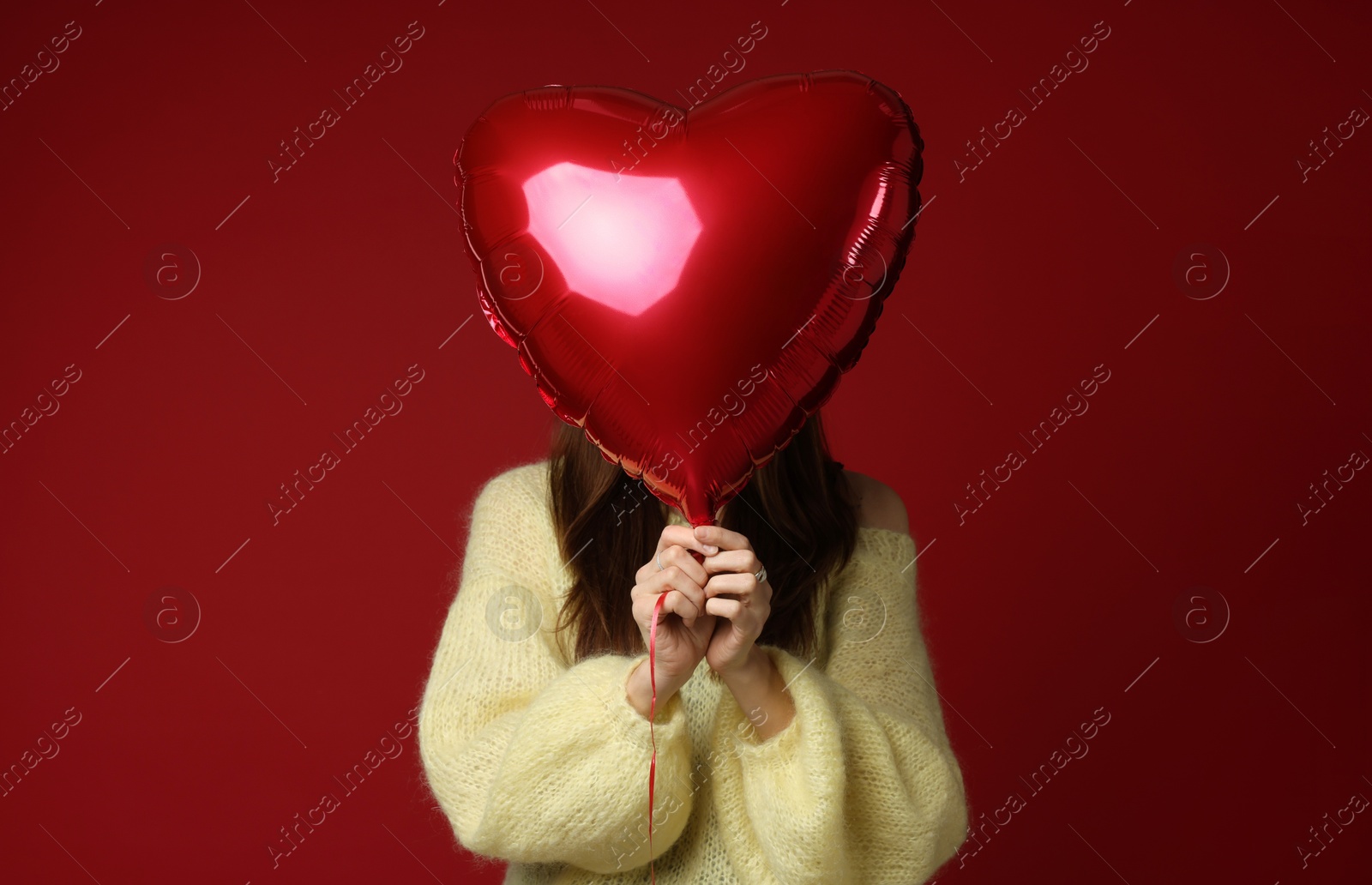 Photo of Happy Valentine's Day. Woman hiding behind heart shaped balloon on red background