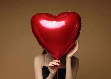 Photo of Happy Valentine's Day. Woman hiding behind heart shaped balloon on brown background