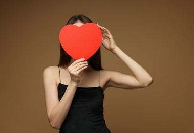 Photo of Happy Valentine's Day. Woman hiding behind paper heart on brown background