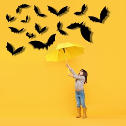 Image of Cute little girl protecting herself from black bats with umbrella on yellow background