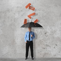 Image of Businessman protecting himself from falling bricks with umbrella on grey textured background