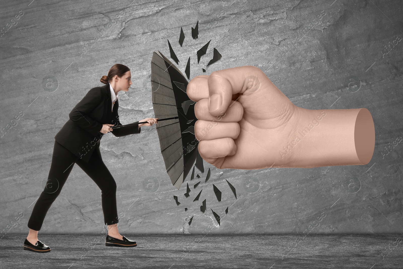 Image of Businesswoman protecting herself from big fist with umbrella on grey textured background