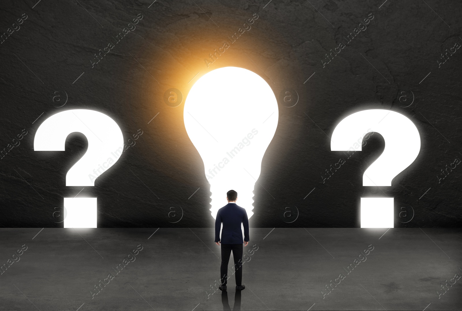 Image of Businessman looking at glowing light bulb and question marks on dark stone wall. Idea, successful strategy