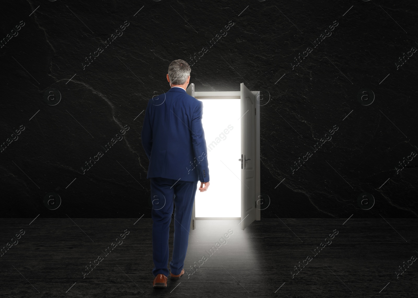 Image of Businessman walking towards open door in dark stone wall. Idea, way to success