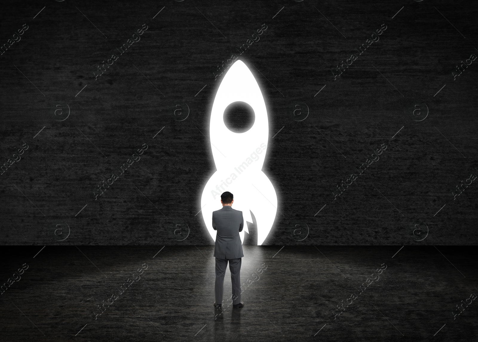 Image of Businessman looking at glowing rocket on dark stone wall. Idea concept