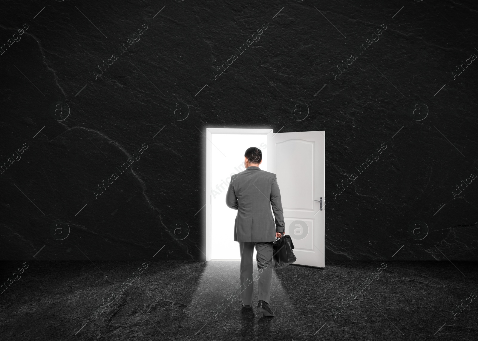 Image of Businessman walking towards open door in dark stone wall. Idea, way to success