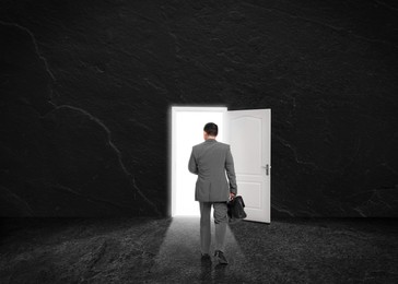 Image of Businessman walking towards open door in dark stone wall. Idea, way to success