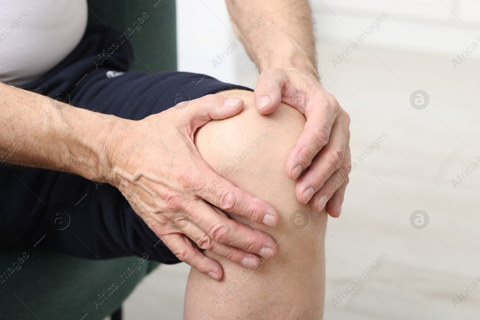 Photo of Senior man suffering from pain in his knee on sofa indoors, closeup