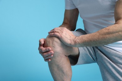 Photo of Senior man suffering from knee pain on light blue background, closeup