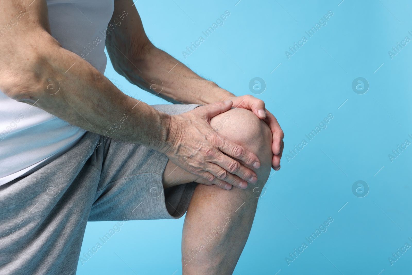 Photo of Senior man suffering from knee pain on light blue background, closeup. Space for text