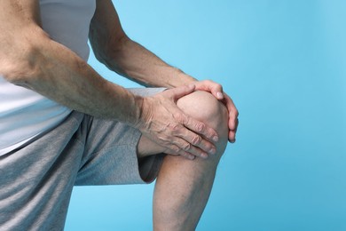 Photo of Senior man suffering from knee pain on light blue background, closeup. Space for text