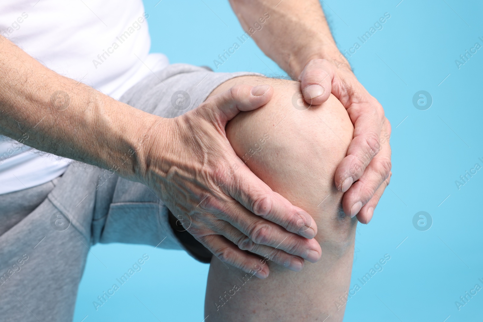 Photo of Senior man suffering from knee pain on light blue background, closeup